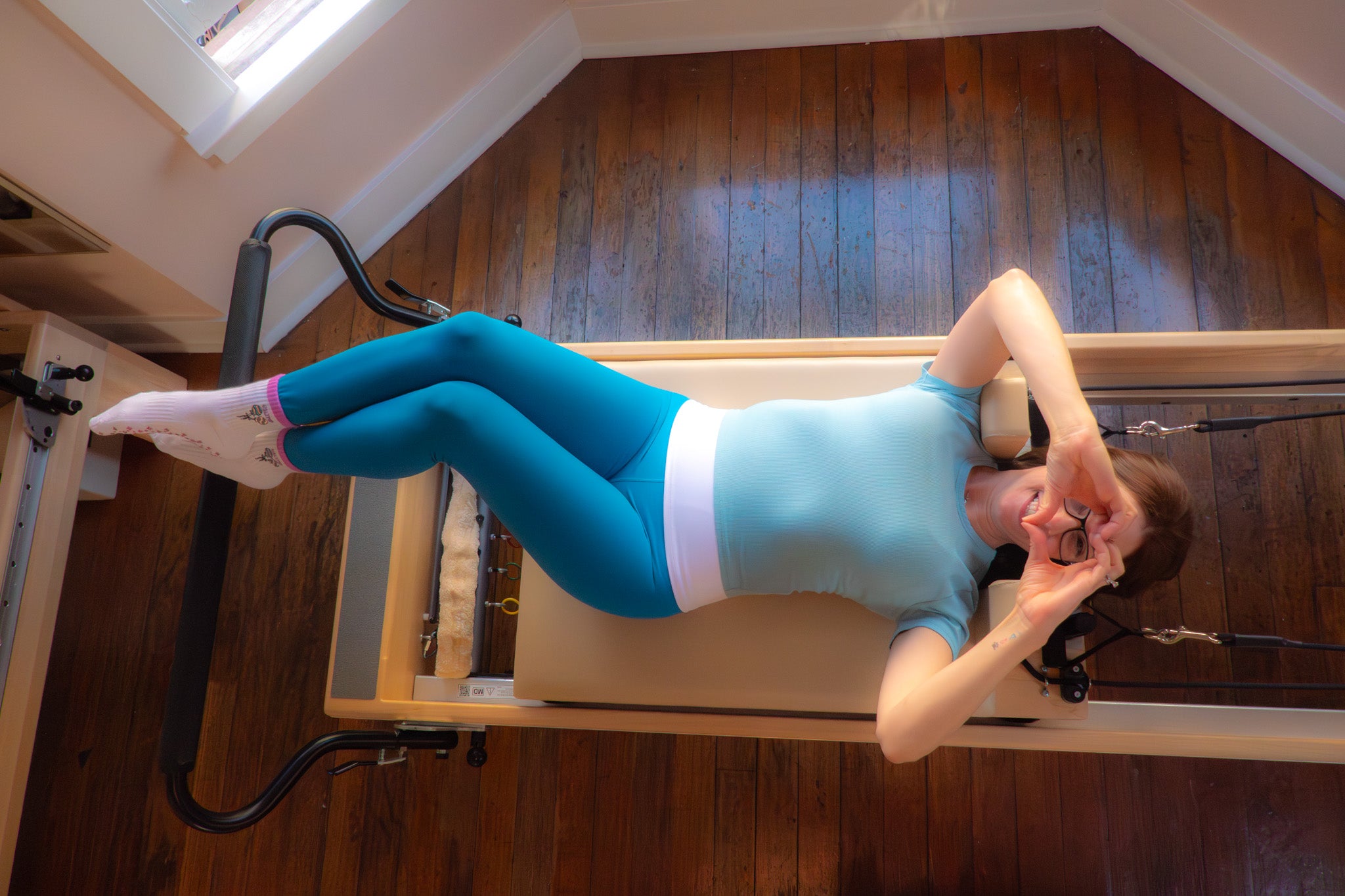 Woman in blue athletic wear on a Pilates reformer on a wooden floor.