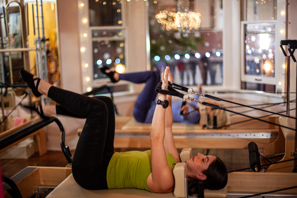 Two women working out on Pilates reformers with a bay window in the background